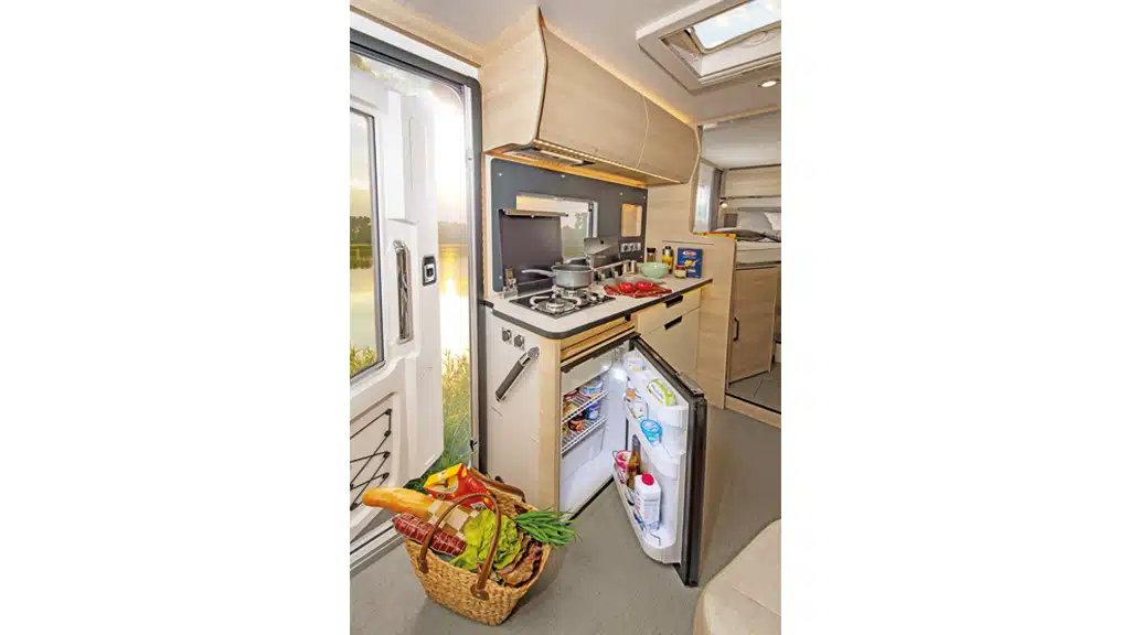 Die Küchenzeile mit elektrischem Dunstabzug und 85-Liter-Kühlschrank. Hinter dem Küchenmodul ist ein Fenster.