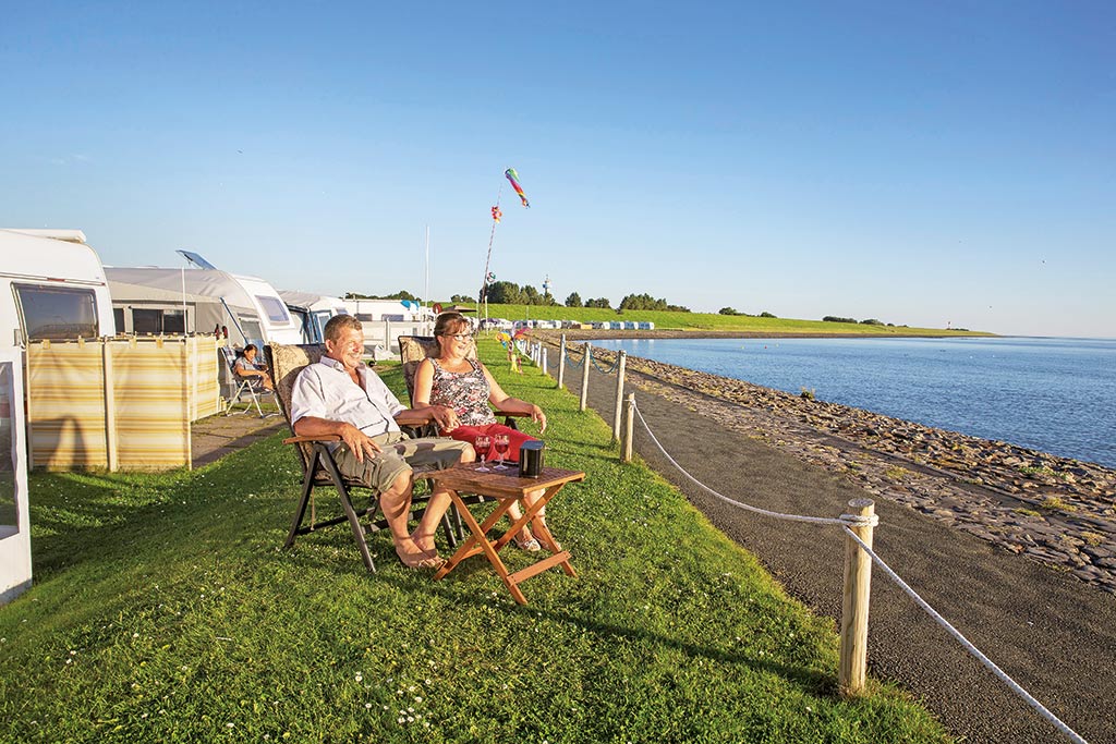 Frau und Mann auf Campingstühlen vor einem Wohnwagen am Nordseedeich