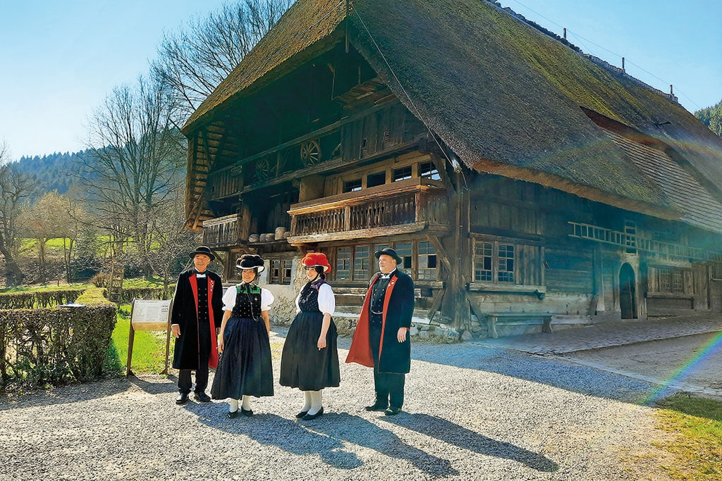 Zwei Paare in Schwarzwälder Tracht vor typischem Schwarzwaldhaus