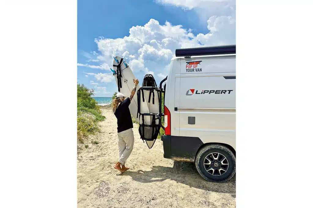 Eine Frau hebt ein Surfbrett vom Heckträger eines Reisemobils