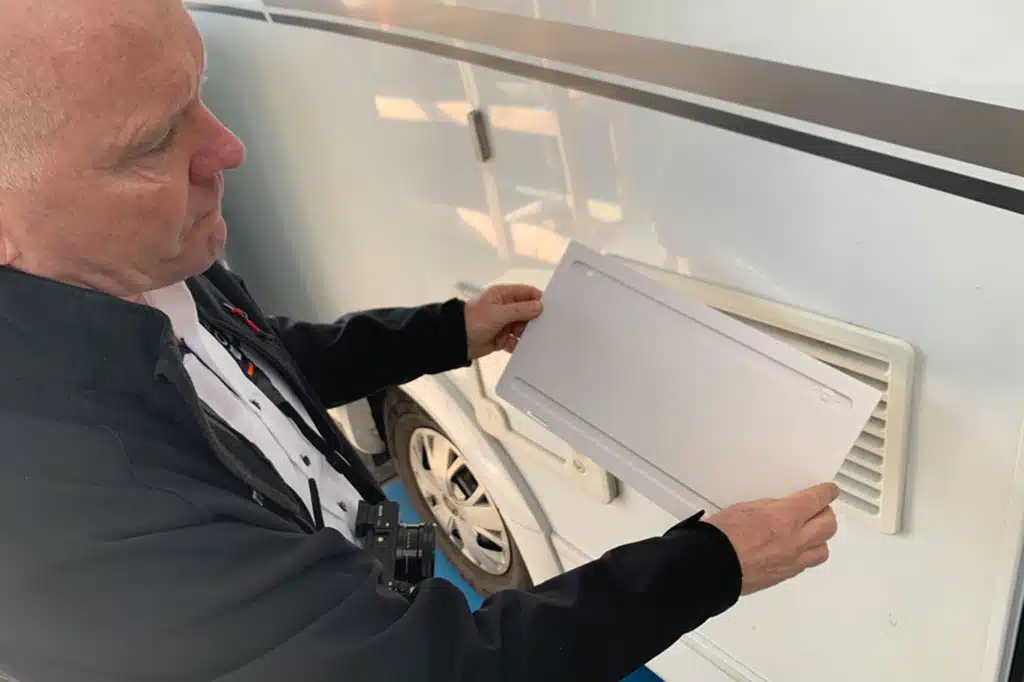Mann montiert eine Abdeckung über dem Kühlschrank-Lüftungsgitter eines Reisemobils