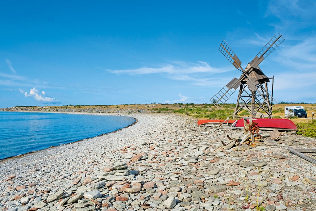 Felsige Küste mit kleiner Windmühle, im Hintergrund ein geparktes Wohnmobil