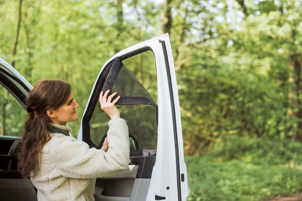 EIne Frau entfernt ein Moskitonetz am Beifahrerfenster eines Fahrzeugs