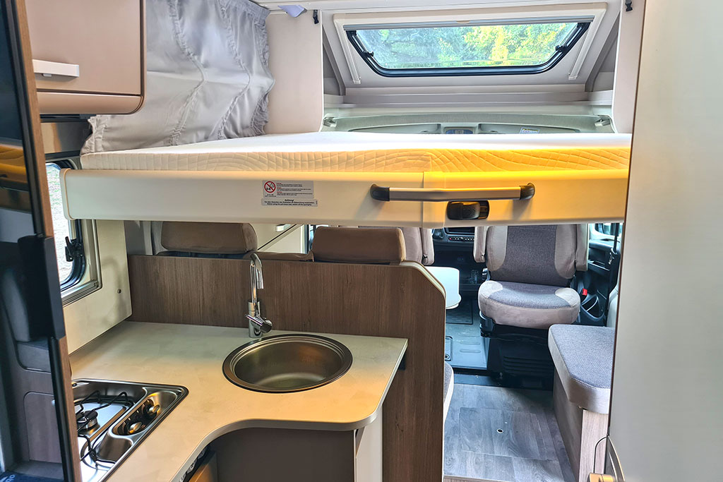 Carado T328 Pro+: Wohnraum im Wohnmobil mit herabgelassenem Hubbett, Sitzgruppe vorne und L-Küche dahinter
