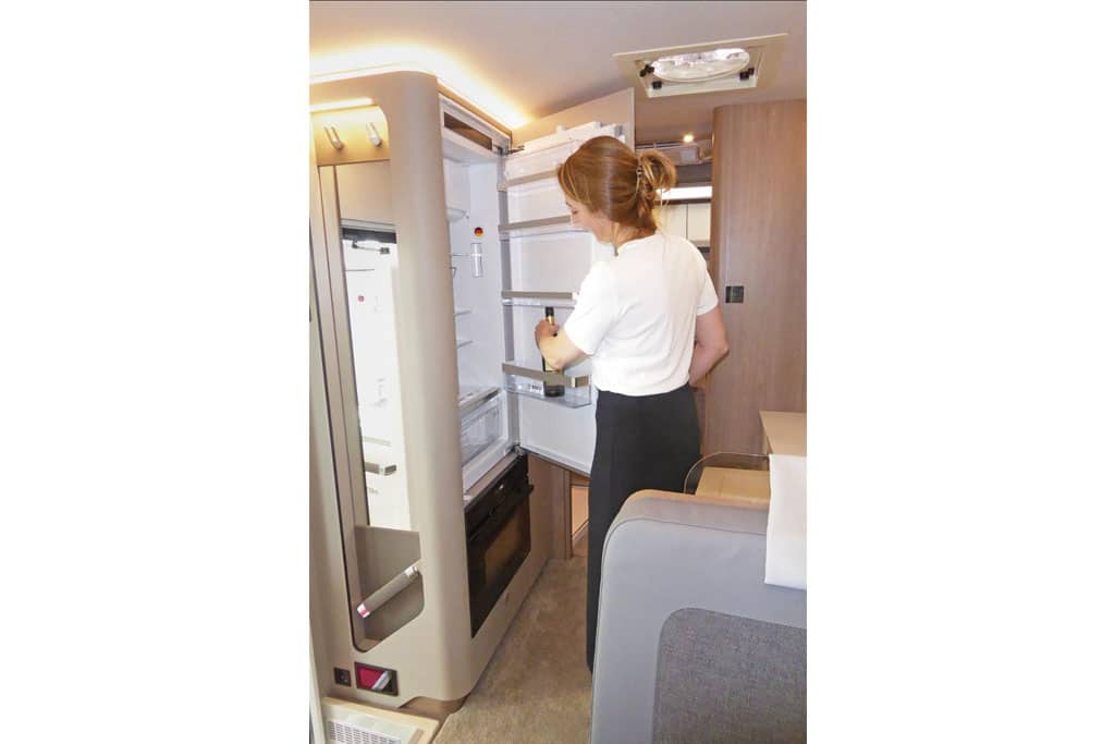 Eine Frau stellt eine Flasche in den großen Kühlschrank des Wohnmobils