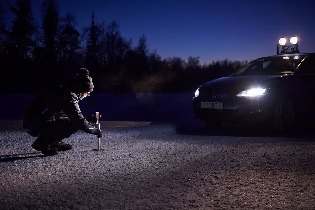 Winterreifentest 2025 -Durchführung: Eine Person misst etwas auf verschneitem Weg vor einem Auto aus.