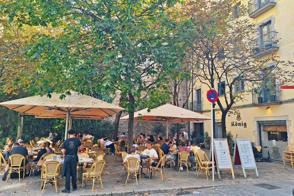 Straßencafé mit Gästen unter Schatten spendenden Bäumen