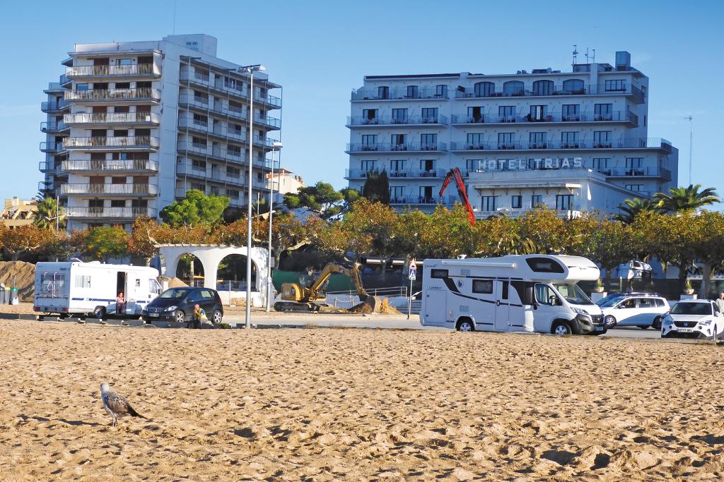 Einige Wohnmobile auf einem Parkplatz hinter einem breiten Sandstrand, im Hintergrund Hochhäuser